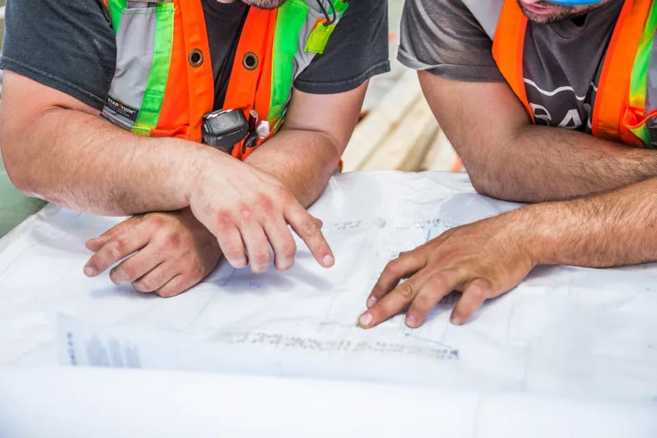 Construction team in high-visibility vests reviewing blueprints together.